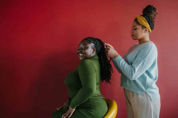 自信的非洲理发师把头发编织成红底美女的辫子 — 图库照片