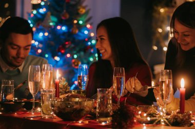 Birlikte yemek masasında otururken Noel arifesinin tadını çıkaran mutlu gençler.