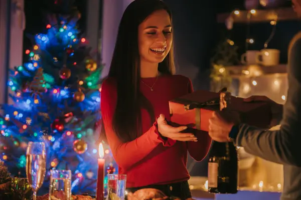 Smiling young woman receiving gift box from boyfriend while enjoying New Year Eve at home