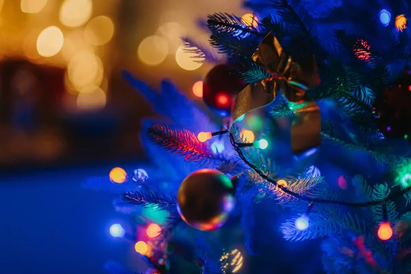 バックグラウンドのガーランドから暖かいボケとクリスマスツリーに掛かる装飾のクローズアップナイトショット — ストック写真