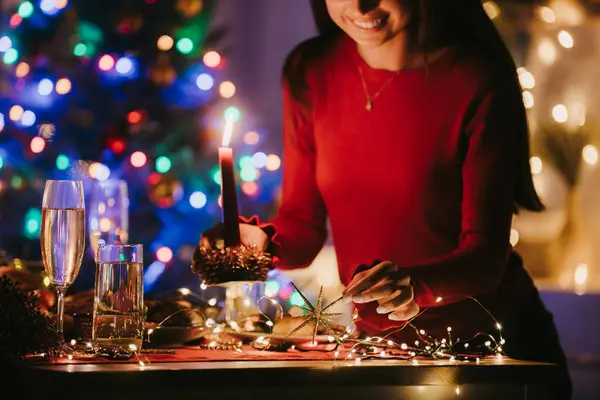 笑顔の若い女性は自宅での新年の祝賀のために準備しながら装飾の休日のテーブルを飾ります — ストック写真