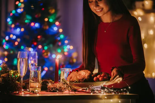 自宅でお正月のお祝いを準備しながらテーブルに休日の料理を提供する笑顔の若い女性 — ストック写真