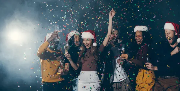 Group of young joyful people dancing and throwing confetti while enjoying New Year party in night club