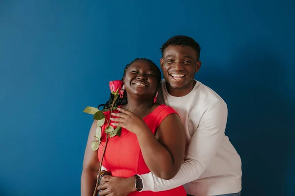 Feliz Joven Africano Abrazando Novia Sosteniendo Rosa Roja Sobre Fondo — Foto de Stock