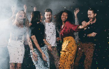 Gece kulübünde kutlama yaparken dans edip konfeti atan bir grup neşeli genç arkadaş.
