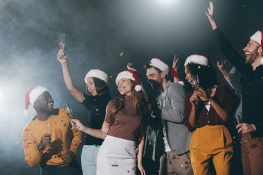 Bir grup mutlu genç gece kulübünde yeni yılı kutlarken etrafta konfeti uçuşuyor.