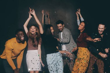 Bir grup neşeli genç gece kulübünde dans edip eğlenirken konfeti uçuşuyor.