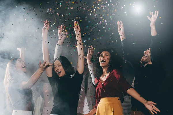 Group of happy young friends dancing and throwing confetti while enjoying celebration in night club