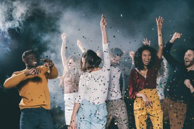 Bir grup neşeli genç gece kulübünde dans edip eğlenirken konfeti uçuşuyor.