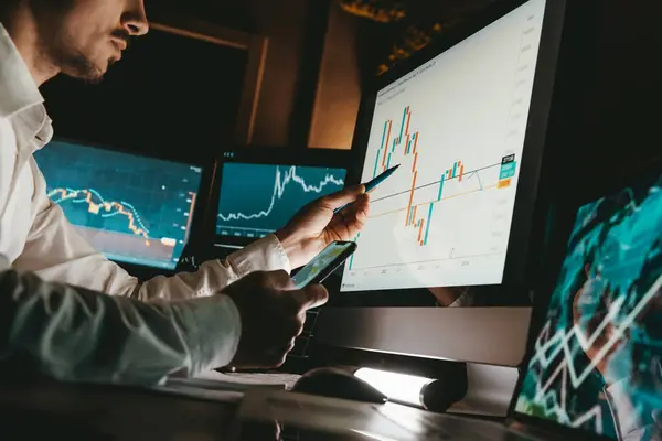 Close-up of male financial broker pointing computer monitor while analyzing stock market graph in night office