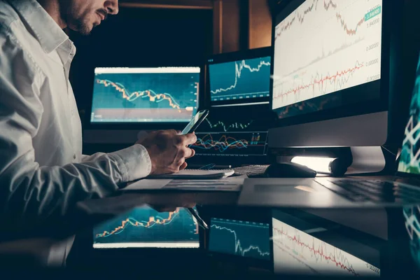 Close-up of male financial broker using technologies while trading on stock market at the night office