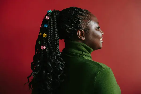 Side view of happy African woman with braided hair and colorful clips standing on red background