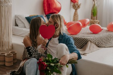 Sevgili çift öpüşüyor ve yüzlerini kalp şeklindeki sevgililer günü kartının arkasına saklıyorlar.