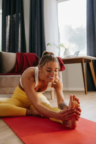 Smiling young woman in sportswear doing stretching exercises during home work out
