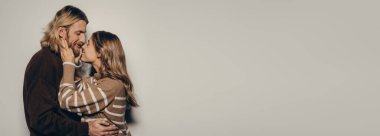 Sıcak, samimi, sevgi dolu genç çift bej arka planda dururken yüz yüze sarılıyorlar.