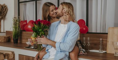 Yakışıklı genç adam sevgililer gününü evde kutlarken kız arkadaşına çiçek veriyor.