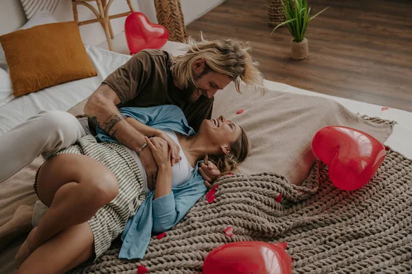 在被红心气球环绕的床上 这对爱玩的夫妻一边拥抱一边玩乐 — 图库照片