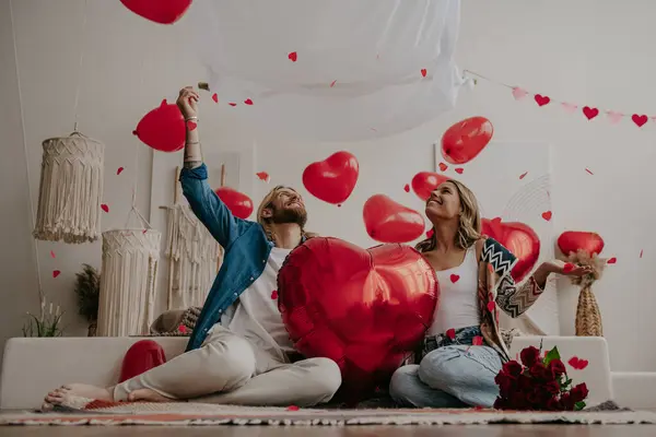 Χαμογελαστό Ζευγάρι Κρατώντας Μπαλόνι Σχήμα Κόκκινης Καρδιάς Και Ρίχνοντας Κομφετί — Φωτογραφία Αρχείου