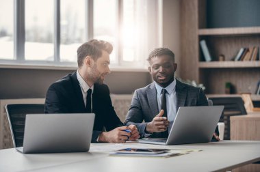 Formalite icabı giyinmiş iki kendine güvenen iş adamı ofiste çalışırken iş konuşuyorlar.