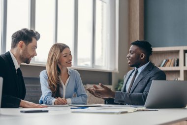 Ofis masasında birlikte otururken üç kendinden emin genç iş görüşmesi yapıyor.