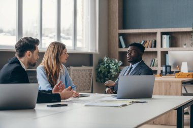 Formalite icabı giyinmiş üç kendinden emin genç ofiste iş konuşuyorlar.