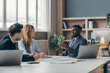 Formalite icabı giyinmiş üç kendinden emin genç ofiste iş konuşuyorlar.