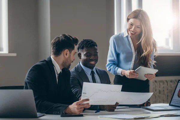 Drei Lächelnde Geschäftsleute Formalbekleidung Analysieren Papierdiagramme Während Sie Gemeinsam Büro lizenzfreie Stockbilder