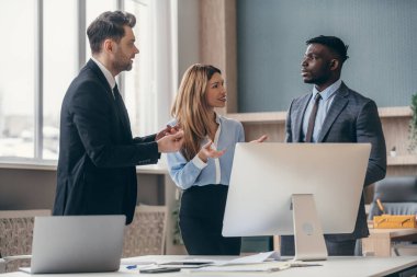 Ofisteki bilgisayarın yanında duran üç kendine güveni tam insan iş hakkında konuşuyor.