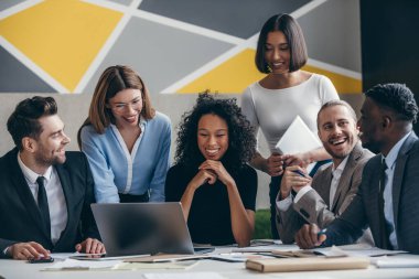 Ofiste grup toplantısı yaparken dizüstü bilgisayara bakan gülümseyen genç iş adamları.
