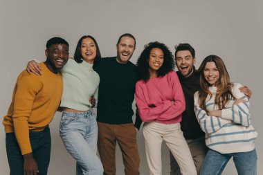 Neşeli genç insanlar bej arka planda birlikte dururken birbirlerine bağlanıp gülümsüyorlar.