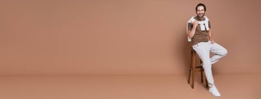 Kahverengi arka planda otururken gülümseyen mutlu genç adam