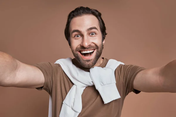 Kahverengi Arka Planda Dururken Selfie Çeken Mutlu Genç Adam — Stok fotoğraf