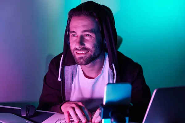 Cheerful young man looking at the computer monitor during live stream against colorful background