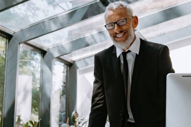 Modern ofisindeki iş yerinin yanında kameraya bakarak mutlu bir iş adamı.