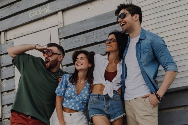 Bir grup neşeli arkadaş yaz gününü birlikte dışarıda geçirirken birbirlerine bağlanıp gülümsüyorlar.