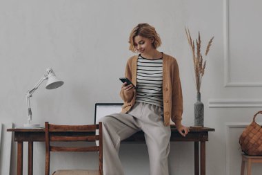 Yaratıcı iş yerinde otururken akıllı telefon kullanan kendine güvenen genç bir kadın.