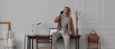 Yaratıcı çalışma yerinde otururken cep telefonuyla konuşan mutlu genç bir kadın.