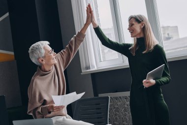 Ofiste yan yana dururken iki mutlu kadın beşlik çakıyor.