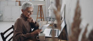 İş yerinde otururken dijital tablet kullanan mutlu kıdemli iş kadını