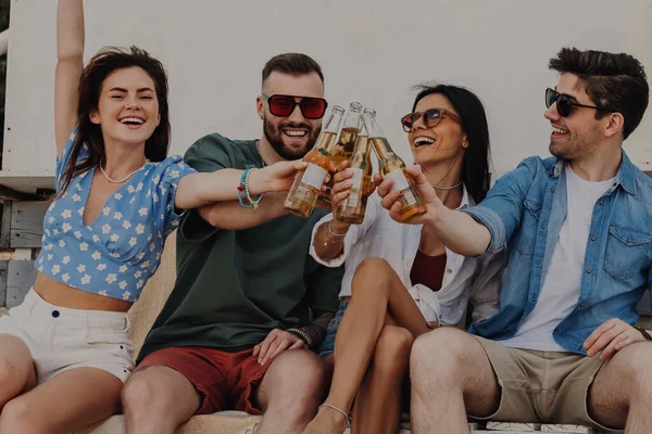 Group of happy friends toasting with beer while spending carefree time outdoors together