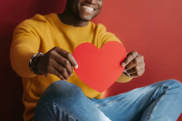 Щасливий Молодий Африканський Чоловік Показує Серцеподібну Листівку Валентина Сидячи Червоному — стокове фото