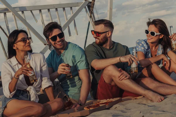 一緒にビーチで時間を過ごしながらピザやビールを楽しむ陽気な若者のグループ ストックフォト