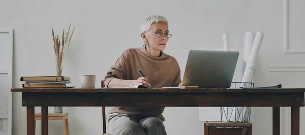 Συγκεντρωμένη Ηλικιωμένη Επιχειρηματίας Που Χρησιμοποιεί Φορητό Υπολογιστή Ενώ Κάθεται Στο Royalty Free Εικόνες Αρχείου