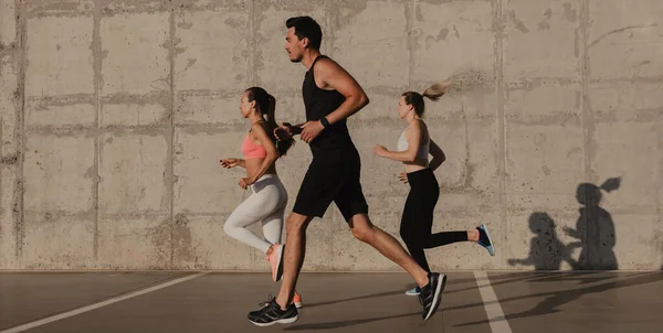 Drei Selbstbewusste Junge Leute Sportkleidung Laufen Gemeinsam Vor Der Betonwand lizenzfreie Stockbilder