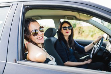 Kameraya gülümseyen ve araba yolculuğunu düşünen iki kadın..