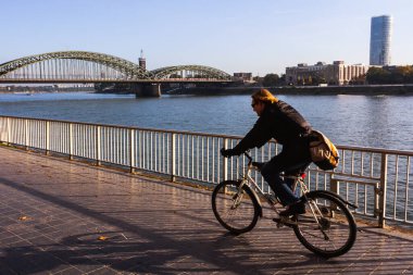 Köln, Almanya - 25 Şubat 2015: Ren nehri yakınlarında bisiklet süren bir bisikletçi. Arka planda Hohenzollern Köprüsü.