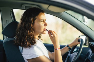 Güzel esmer bir kadının arabanın dikiz aynasına bakarken ruj sürdüğü profil pozu. 