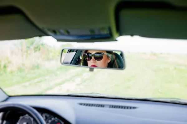 Reflection in the car\'s rear-view mirror of an elegant woman while driving