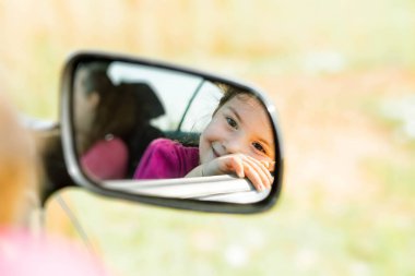 Pose of a nice child who is smiling in the car's mirror.