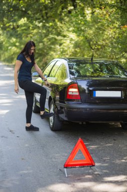 Bir kadın yolun kenarında arızalı olarak arabasına bakıyor..